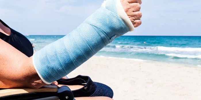 a tourist sat on a beach with their arm in a cast