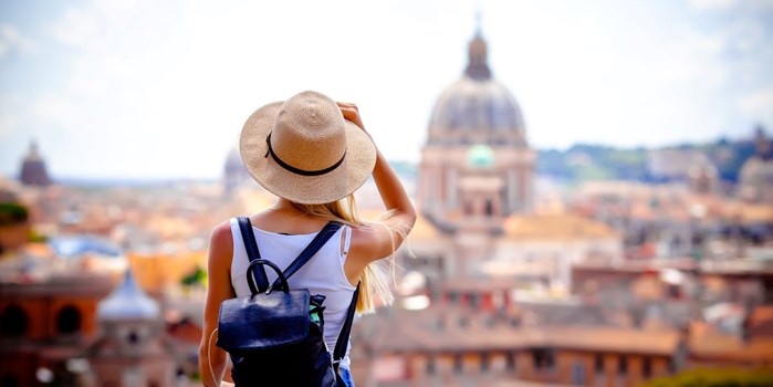 Young tourist wearing a hat and backpack taking in a view of a city in the sun 